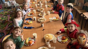 Dzieci siedzące przy stolei zajadają się przygotowanym poczęstunkiem.