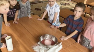 Dzieci stojące do okoła stołu z przyborami do eksperymentu
