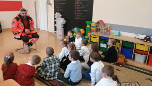 Dzieci siedzą w półokręgu i słuchają wypowiedzi ratownika medycznego