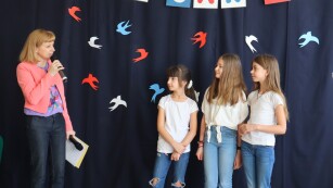 Nauczycielka przedstawia trzy uczennice - wokalistki.