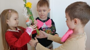 Dwóch chłopców wręcze prezent oraz kwiaty koleżance w czerwonej sukience