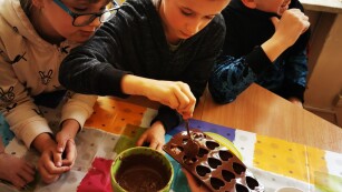 Uczeń nalewa płynną czekoladę do foremek w kształcie serduszek.