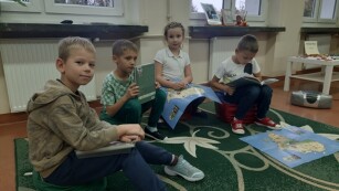 Grupa przedszkolaków siędząca na dywanie w sali i pozująca do zdjęcia, z audiobookami w rękach - SPOTKANIA Z AUDIOBOOKIEM