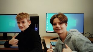Dwaj uczniowie przy stanowisku komputerowym unoszą kciuki w górę