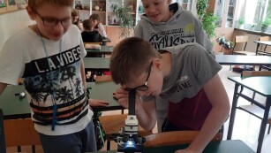 Jeden uczeń patrzy przez mikroskop, dwaj inni się przyglądają mu