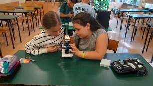dwie dziewczynki siedzą przy mikroskopie