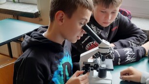 Jeden z uczniów patrzy przez mikroskop, drugi siedzi obok