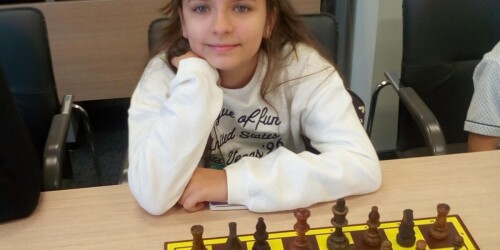 Uczennica siedzi przy planszy z szachami i czeka na rozpoczęcie gry.