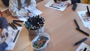 Uczniowie przy stoliku kolorują kolorowanki-skarpetki.