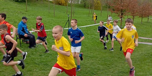 Uczniowie biegną wyznaczona trasą po trawie.